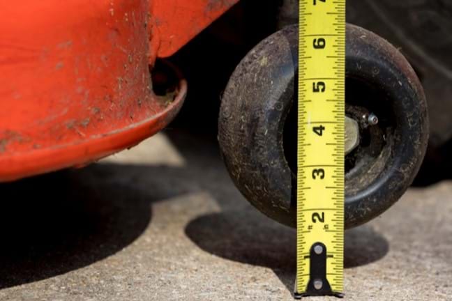 close up of a mower wheel being lifted and a measuring tape being held out and perpendicular to the ground - testing mower height